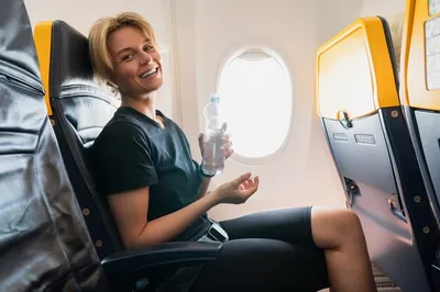 Молодая и счастливая женщина пьет воду во время полета в самолете | Премиум  Фото